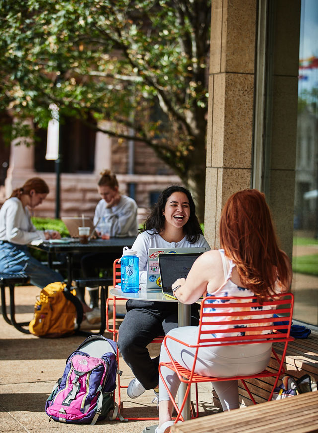 Students at tables outside of the library, smiling and talking while studying