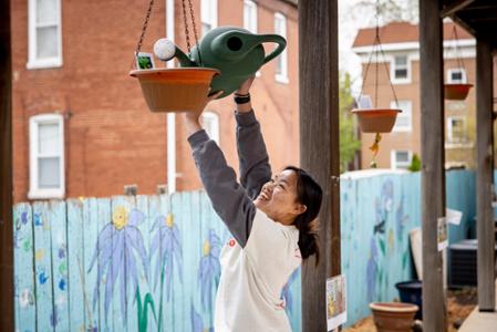 A student stretches her arms to water a plant pot at a volunteer site.
