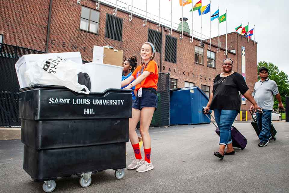 Student helping new 91女神 family move in, pushing cart to residence hall