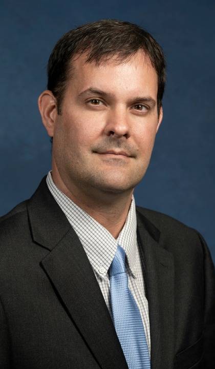 Steven Winton headshot, wearing dark suit, light shirt and light blue tie.
